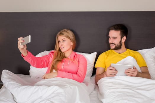Young happy couple on bed doing selfie with telephone camera. Concept about technology and people
