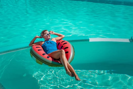 Happy woman in a swimsuit and sunglasses floating on an inflatable ring in the form of a watermelon, in the pool during summer holidays and vacations. Summer concept