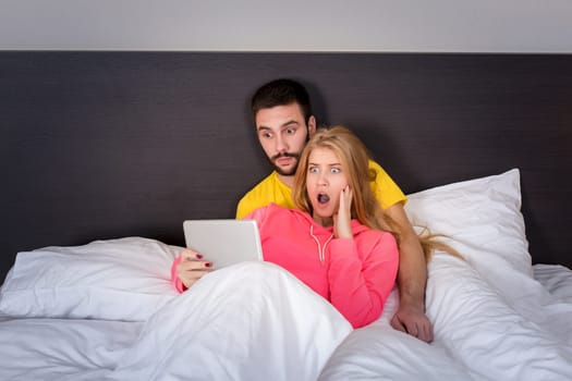 Young Sweet Couple on Bed Watching Something on Tablet Gadget. Concept about technology and people