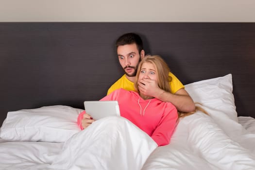 Young Sweet Couple on Bed Watching Something on Tablet Gadget. Concept about technology and people