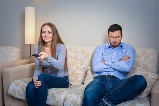 Portrait of couple sitting on sofa watching television. Image of hapy woman with remote control in hands and upset man