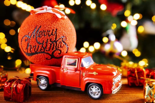 Red retro toy truck with Christmas balloon and gift boxes on wooden table with Christmas lights background. Christmas and new year greeting card. Selective focus