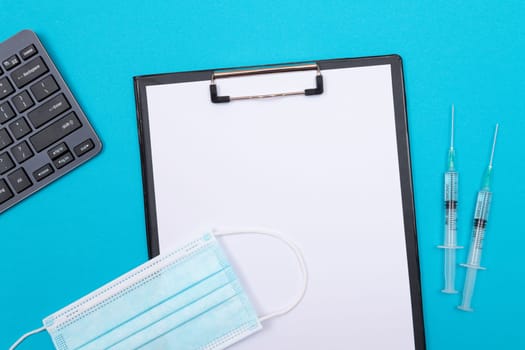 Vaccination, Immunology or Revaccination Concept - Two Medical Syringe Lying on Blue Table in Doctor's Office in a Hospital or Clinic. Black Clipboard with Sheet of Paper - Mock Up with Copy Space