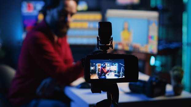 Content creation equipment used by photo editor to film tutorial on selecting editorial pictures for fashion magazine. Focus on camera recording photographer in blurry background presenting his work