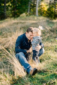 Sitting dad hugging a little girl standing next to him in a clearing in the forest. High quality photo