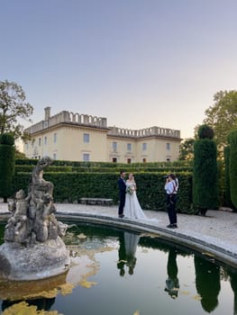 Girl-photographer photographs bride and groom near the fountain in the garden of an old villa. High quality photo