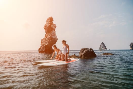 Woman sup yoga. Middle age sporty woman practising yoga pilates on paddle sup surfboard. Female stretching doing workout on sea water. Modern individual hipster outdoor summer sport activity