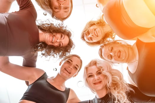 Low angle shot of smiling women looking at the camera, hugging, standing in a circle and doing team building.