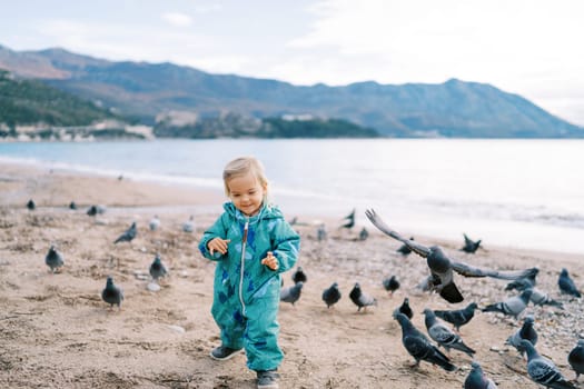 Little smiling girl walks along the seashore among a flock of pigeons. High quality photo