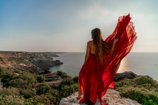 Woman sunset sea red dress, back view a happy beautiful sensual woman in a red long dress posing on a rock high above the sea on sunset