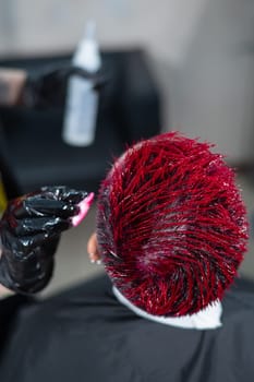 The hairdresser removes excess dye from the skin of a female with a cotton pad.Asian woman with a short haircut in a hairdressing salon