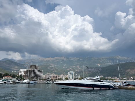 Yacht is moored at the pier with high-rise buildings on the shore against the backdrop of mountains in white clouds. High quality photo