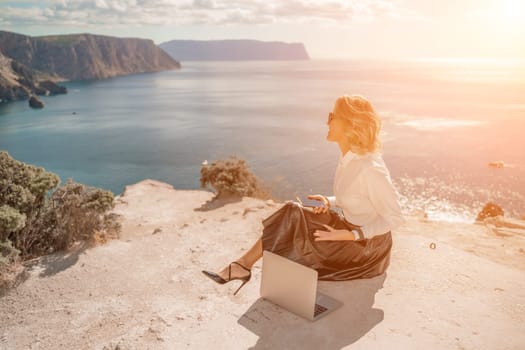 Freelance women sea. She is working on the computer. Good looking middle aged woman typing on a laptop keyboard outdoors with a beautiful sea view. The concept of remote work