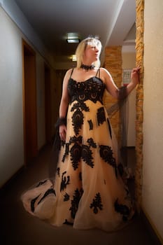 Full length view of a blonde female model, dressed in a black and white queen dress in dark corridor. Mysterious stranger alone inside castle or hotel