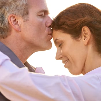 Couple, forehead kiss and hug with love, respect or happiness on holiday in romance. Mature, man and woman embrace together outdoor at sunset on vacation or show affection or gratitude in marriage.