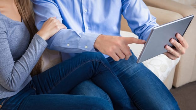 Couple bvsitting on a sofa with electronic table. Close shot of male hands holding a tablet in hands