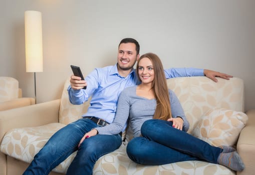 Portrait of happy couple sitting on sofa with remote control in hands and watching television together