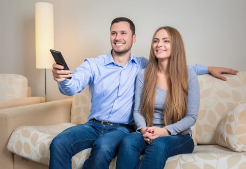 Portrait of happy couple sitting on sofa with remote control in hands and watching television together