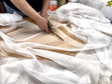 Women's hands with scissors cut the chiffon fabric. A seamstress cuts clothes. The seller prepares fabric for sale