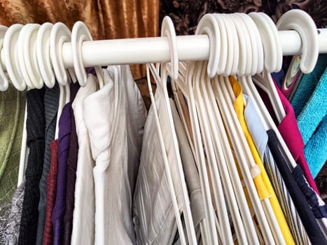 Hangers with a variety of clothes on white rack. Home storage of clothes. Clutter. Littery. Declutter. Garage sale