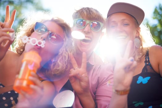 Portrait, peace sign and happy friends in sunglasses outdoor, blowing bubbles and funny laugh together in summer. Face, women and group of girls with v hand gesture, excited and lens flare in nature.