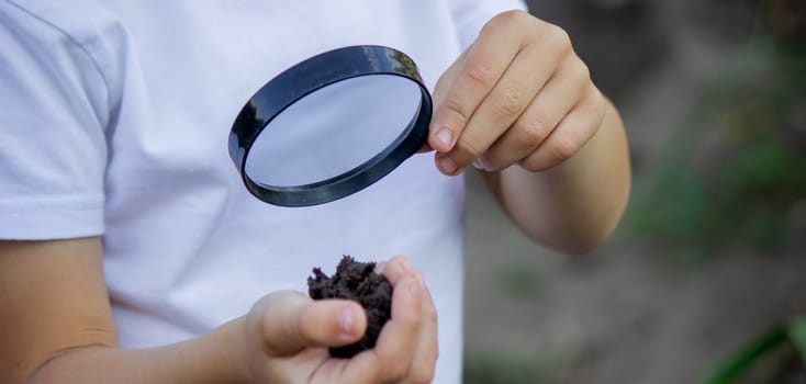 The child examines the ground with a magnifying glass. Selective focus. Nature.