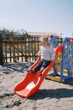 Little girl slides down a slide on the playground holding onto the handrails. High quality photo