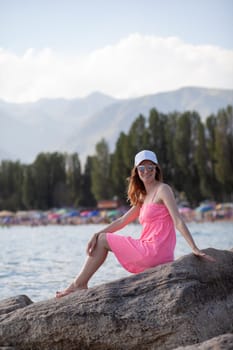 A beautiful girl in a red swimsuit with long hair, glasses and a white cap looks at the blue sea.