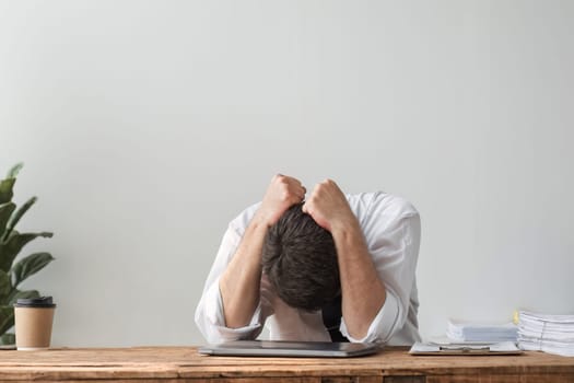 Unhappy young businessman feeling bored and stressed at work looking at laptop with hopeless expression while sitting in office.