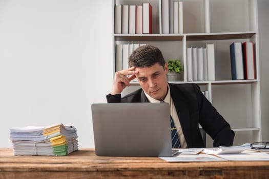 Unhappy young businessman feeling bored and stressed at work looking at laptop with hopeless expression while sitting in office.