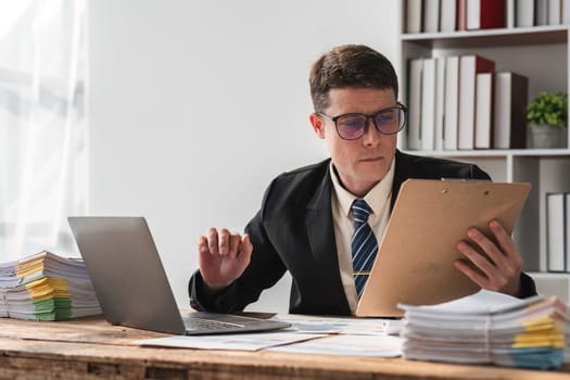 Unhappy young businessman feeling bored and stressed at work looking at laptop with hopeless expression while sitting in office.