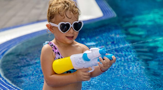 A child plays with a water pistol in the pool. Selective focus. Kid.