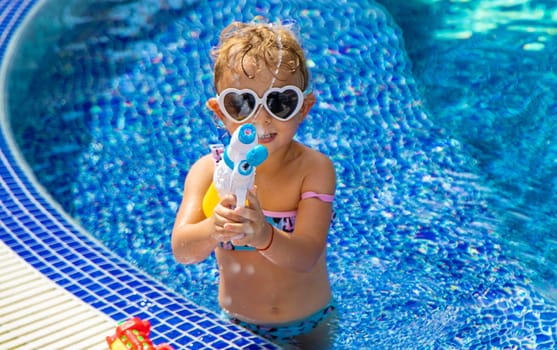 A child plays with a water pistol in the pool. Selective focus. Kid.