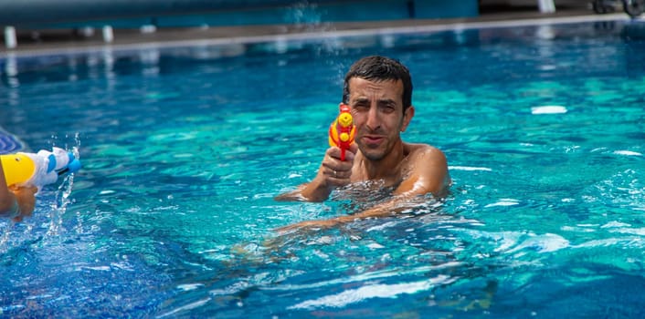 A man plays with a water pistol in the pool. Selective focus. Nature.