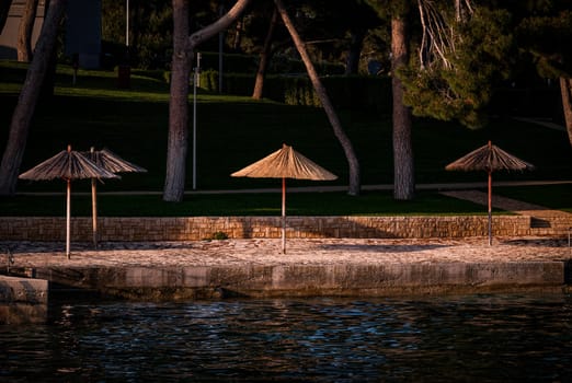 a number of bamboo parasols on a beach in the late evening sun with the sea in the foreground in a holiday paradise