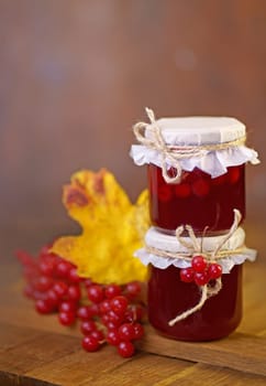viburnum jam. Red juicy berries of a viburnum with sugar in a glass jar on a dark wooden background. For making jam, tea.