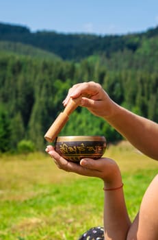 A woman holds a singing bowl in her hands. Selective focus. Nature.