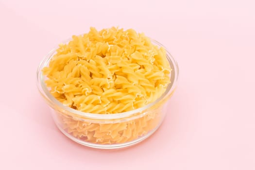 Uncooked Fusilli Pasta in Glass Jar on Pink Background. Fat and Unhealthy Food. Classic Dry Spiral Macaroni. Italian Culture and Cuisine. Raw Pasta