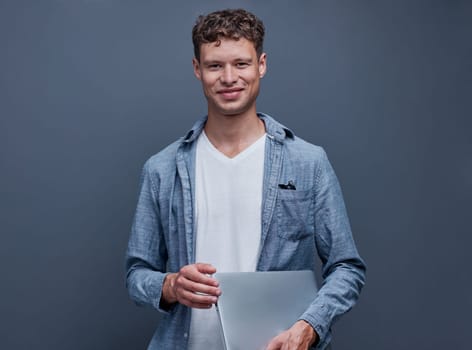young man on gray background holding a laptop.