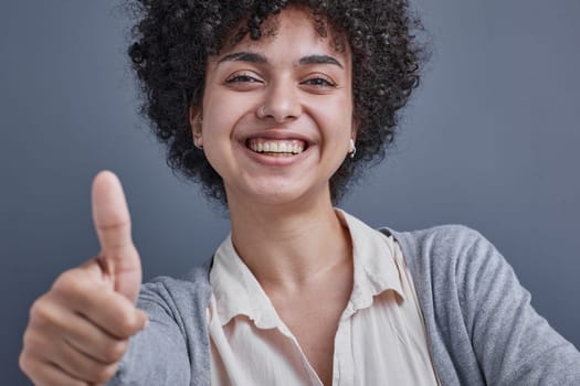 girl on a gray background smiling and showing a raised thumb.