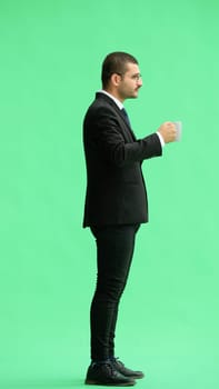 young man in full growth. isolated on green background. holding a mug of coffee.