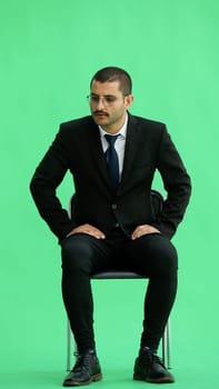 young man in full growth. isolated on a green background sitting on a chair.