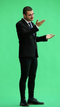 young man in full growth. isolated on green background demonstrates with hands.