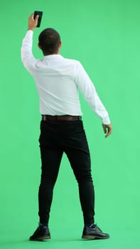 man in full growth. isolated on green background using phone.
