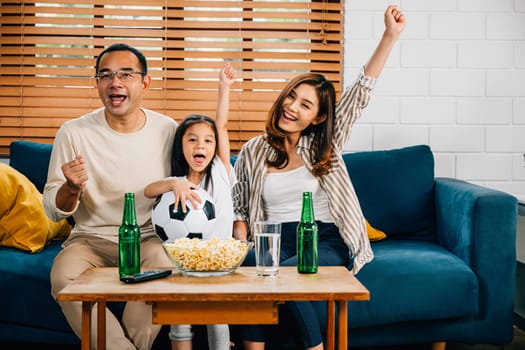 A joyful family and their daughter bond over a football match on TV, celebrating their team's success with cheers and excitement. Their smiles and togetherness fill the room with happiness.
