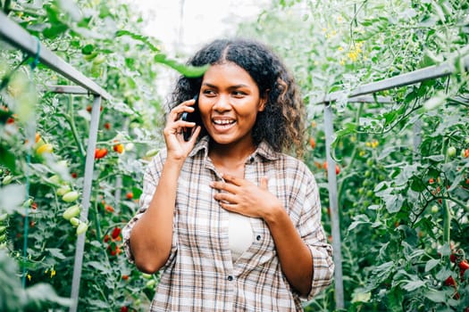 In the fresh air of the greenhouse, a joyful woman farmer talks on her phone, clutching ripe tomatoes. Technology aids farm-to-community communication, nurturing growth and happiness.