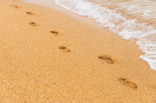 sand, wave and footprints in the daytime. golden sandy beach with sea waves, close-up of solitary human footprints.
