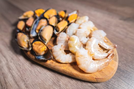 Side view of a plate of mixed seafood being served as an appetizer. Peeled shrimp and mussels in the shell lie on a wooden plate, close-up.