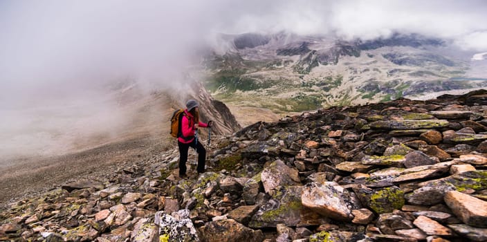 A young woman traveling through the mountains with backpacks on a cloudy day. Climbing the mountain on a cold day and fog, humid environment, panoramic view.