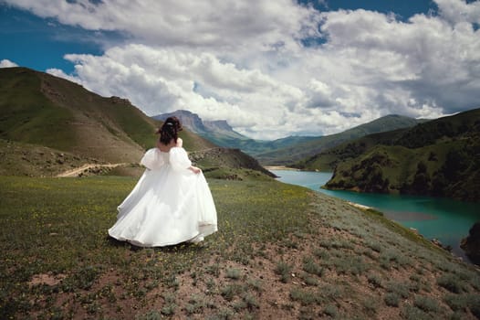 Rear view of a beautiful bride, woman running through the grass on a hill in the mountains while the wind blows her wedding dress. Natural landscapes.